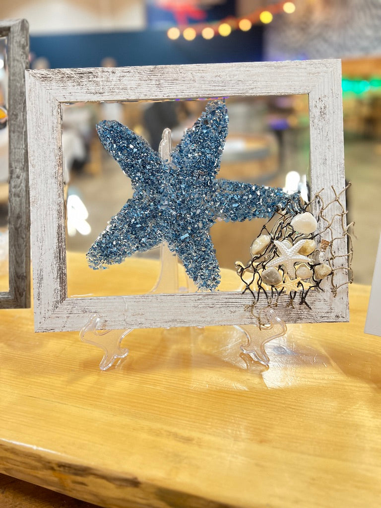Decorative frame with a blue starfish and seashells on a wooden surface.