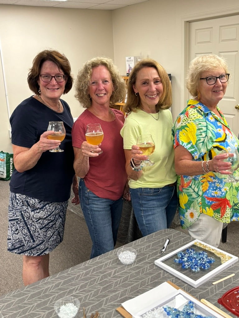 Four women standing together, each holding a glass of wine, in a casual indoor setting.